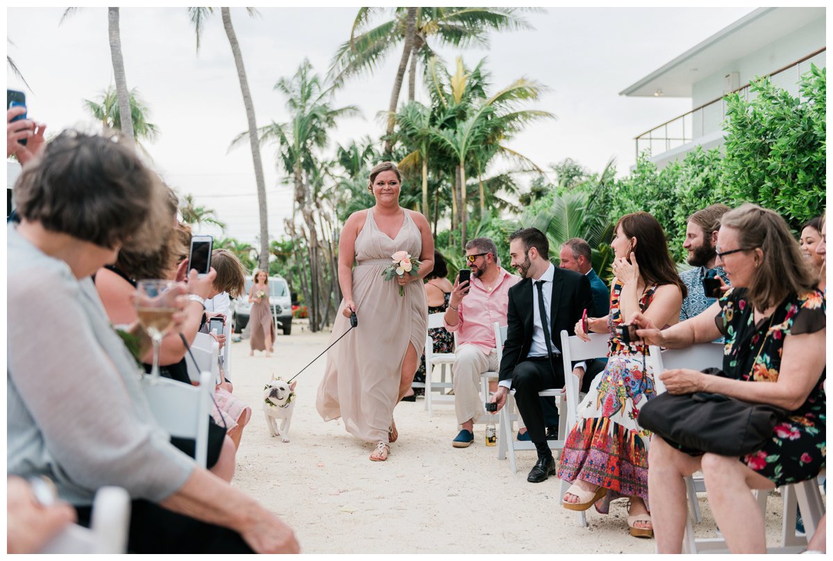 The maid of honor walks the bride's dog down the aisle at their beach wedding